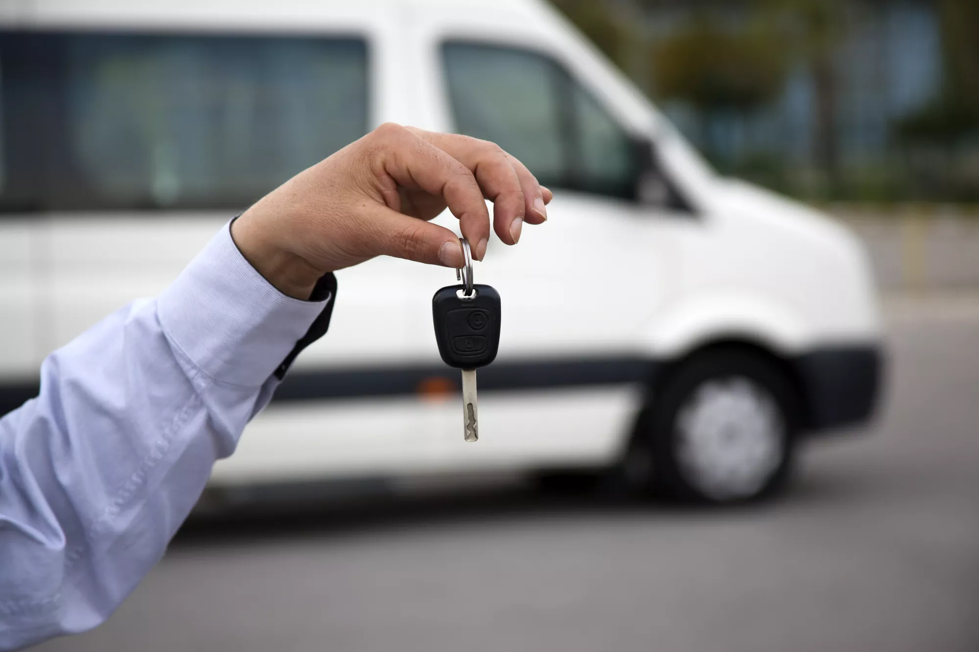 Hand hält einen Autoschlüssel vor einem Kleinbus